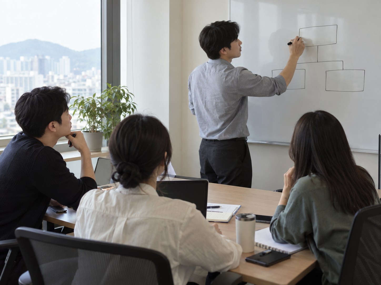 회의가 막히자 한 직원이 먼저 일어나 화이트보드 앞에서 정리를 시작하고 동료들이 앉아서 지켜본다 — 먼저 나서는 버릇은 막힌 일을 풀기도 하고 누군가에게는 부담이 되기도 한다