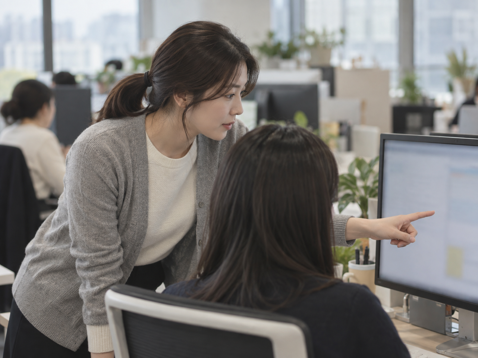 동료 자리 옆에서 몸을 숙여 모니터를 같이 보며 한쪽을 짚어 주는 직장인 — 평소에 동료 일을 조금씩 도와 두면 나를 대신 말해 줄 사람이 생긴다